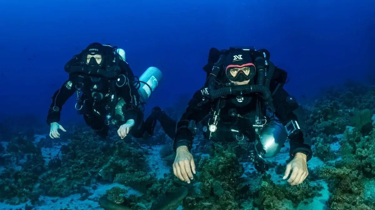 Two closed-circuit rebreather divers gliding over a Red Sea reef in Hurghada