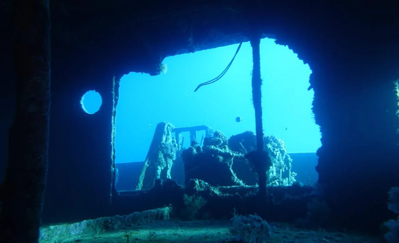 A large opening in the steel hull of an Abu Nuhas shipwreck, open blue water beyond