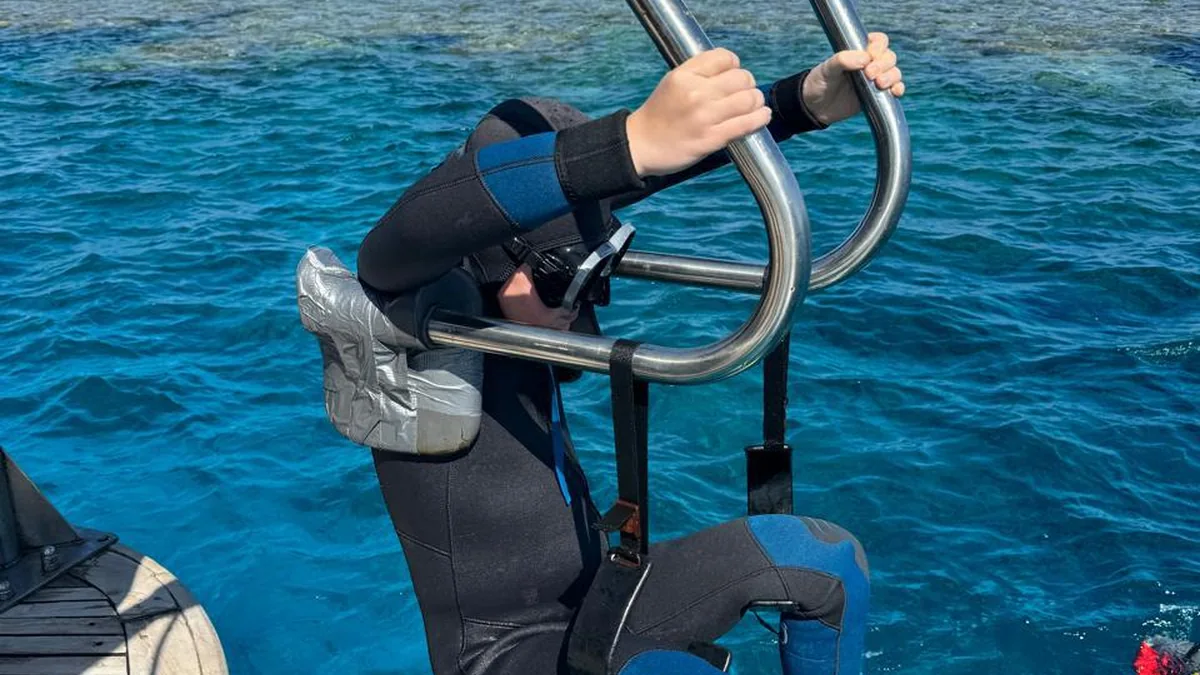 A scuba instructor assists an adaptive diver into the Red Sea from the boat