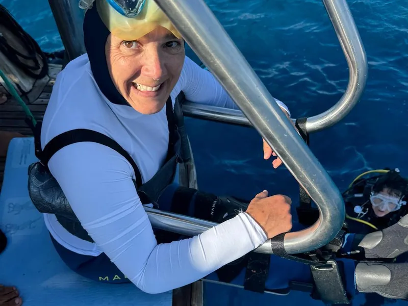 A diver with a disability gliding weightless over a Red Sea reef alongside an instructor, calm and smiling